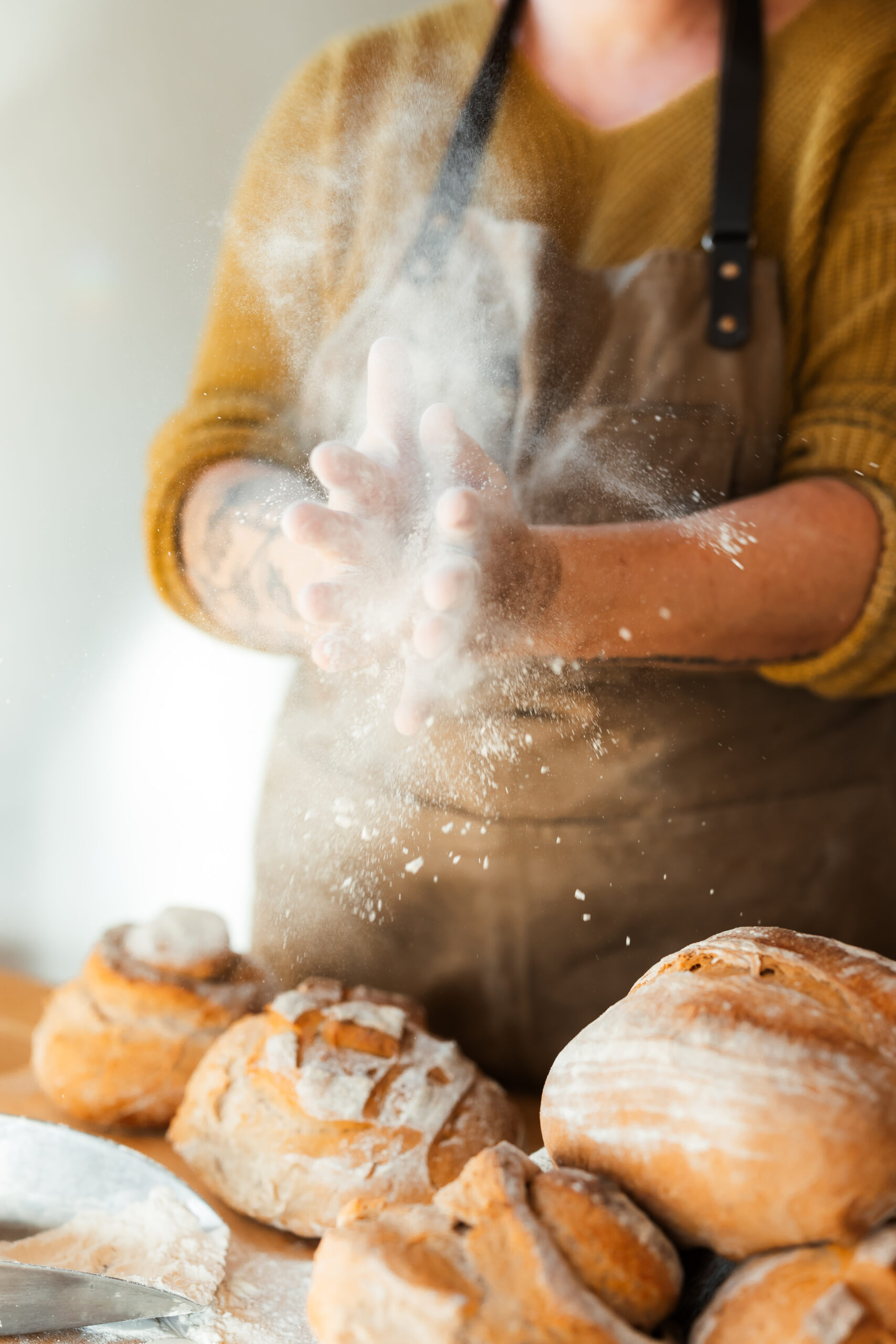 Bäckerin klatscht Mehl von den Händen, im Vordergrund liegen frisch gebackene Brote.